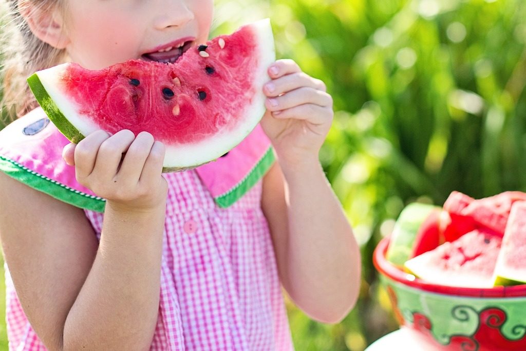 A young girl enjoys the outdoors while eating watermelon.